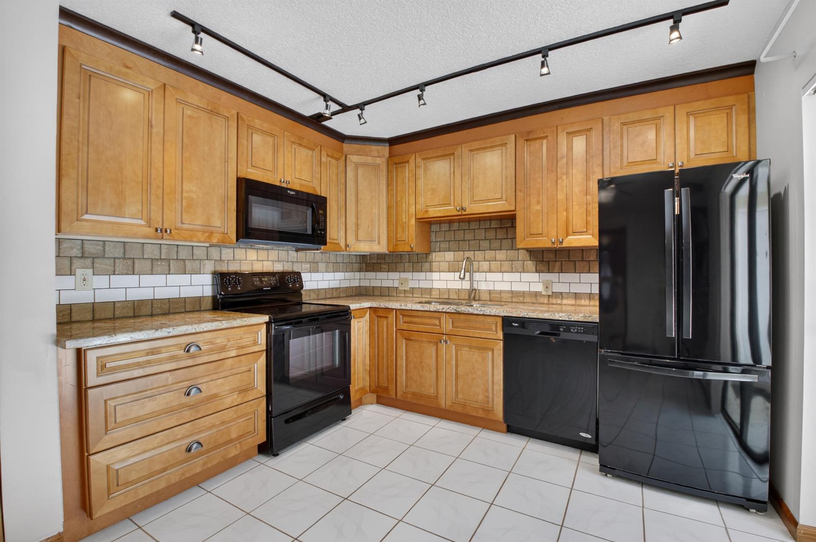 A kitchen features light wood cabinets, black appliances, granite countertops, and a tiled backsplash — 1565 Augusta Circle # 103, Delray Beach FL 33445, DELRAY BEACH, FL