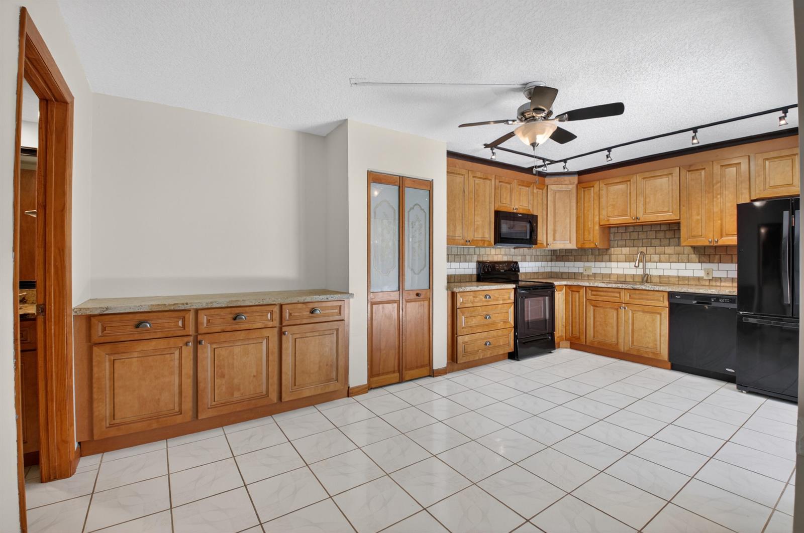 A kitchen features light wood cabinets, black appliances, a granite countertop, and white tile flooring — 1565 Augusta Circle # 103, Delray Beach FL 33445, DELRAY BEACH, FL