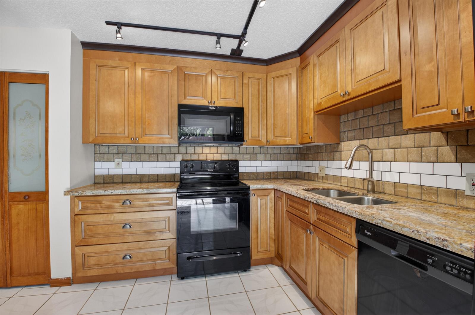 A kitchen features wood cabinets, granite countertops, a black stove, and a tiled backsplash — 1565 Augusta Circle # 103, Delray Beach FL 33445, DELRAY BEACH, FL
