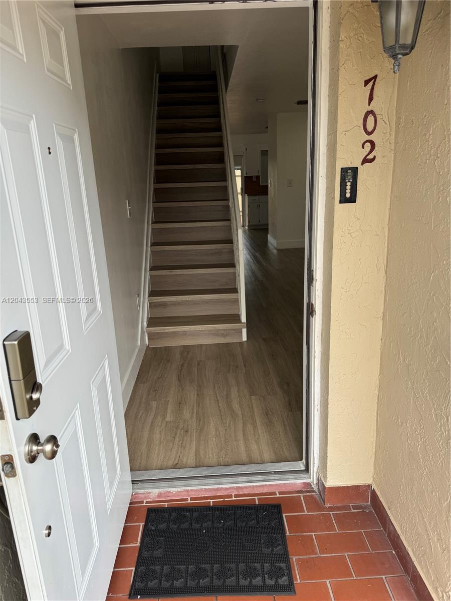 An open front door reveals a staircase and wood-look flooring leading to a kitchen area — 6250 SW 130th Ave # 702, Miami FL 33183, MIAMI, FL