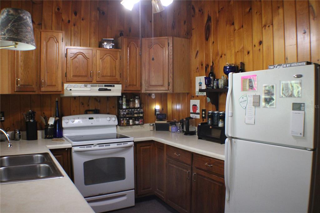 A kitchen with wood-paneled walls, oak cabinets, white appliances, and a double-basin sink — 3045 YORKSHIRE DRIVE, DELTONA, FL