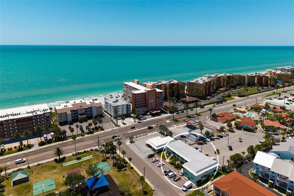 An aerial view shows a low-rise building circled in white near a coastal road — 10 164TH AVENUE UNIT 1, REDINGTON BEACH, FL