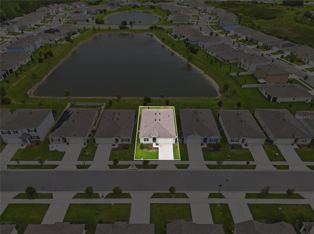 An aerial view shows a single-family home with a white outline situated near a pond — 995 BROOKLET DR, DAVENPORT, FL
