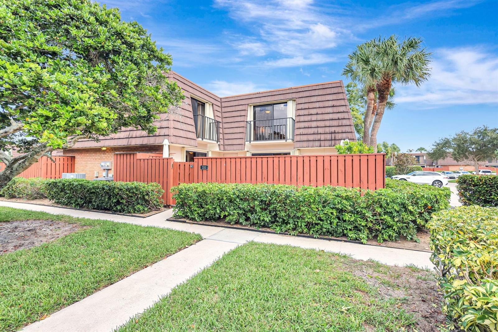 A two-story townhouse with a brown mansard roof, a wooden privacy fence, and landscaping — 2332 23rd Court # 57d, Jupiter FL 33477, JUPITER, FL