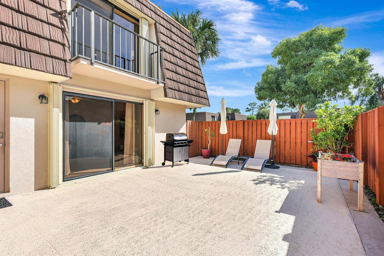 A concrete patio features a grill, two lounge chairs with umbrellas, and a wooden planter — 2332 23rd Court # 57d, Jupiter FL 33477, JUPITER, FL