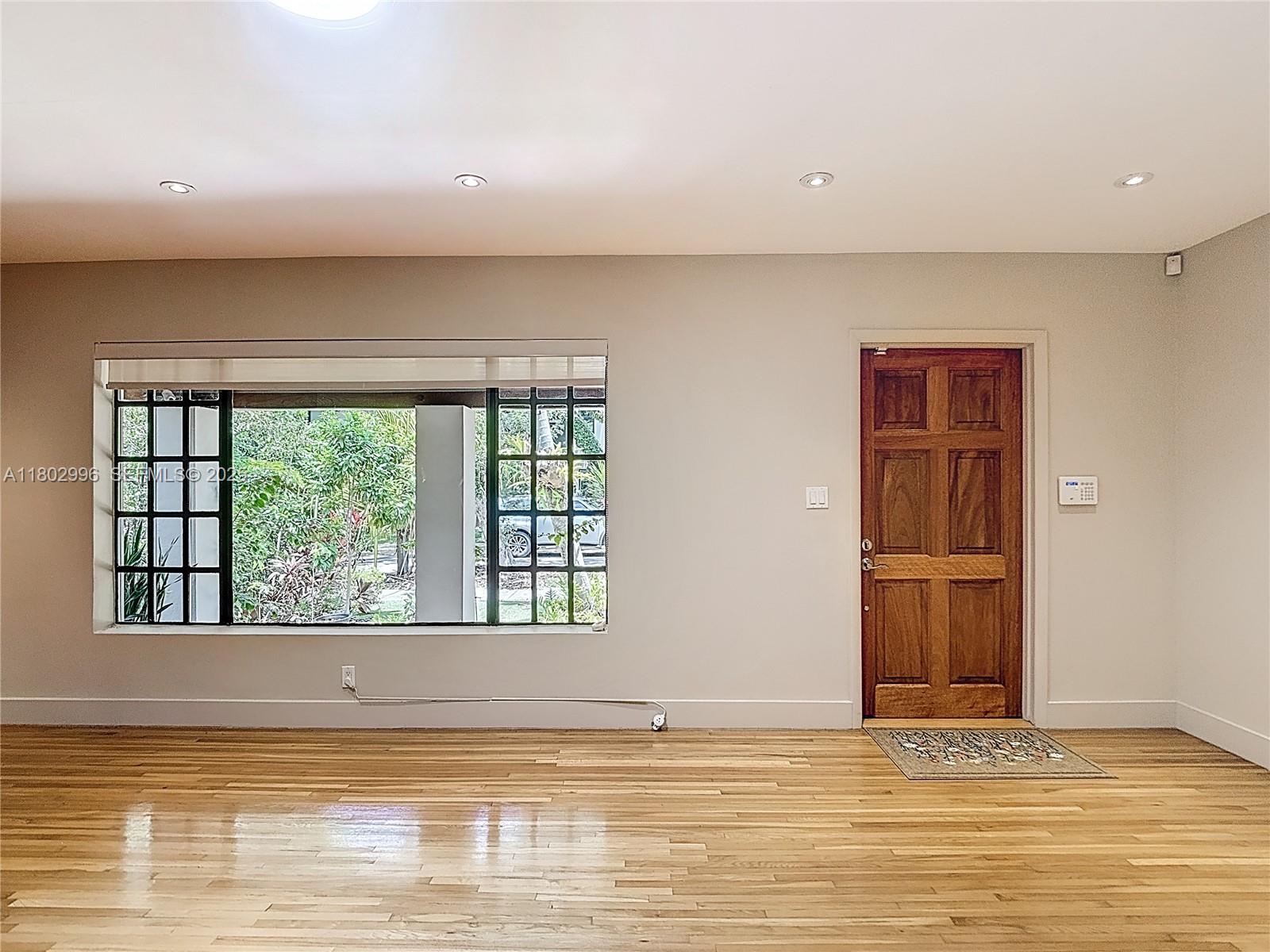 A room with hardwood floors, a large window with grid panes, and a wooden front door — 2810 Crystal Ct, Miami FL 33133, MIAMI, FL