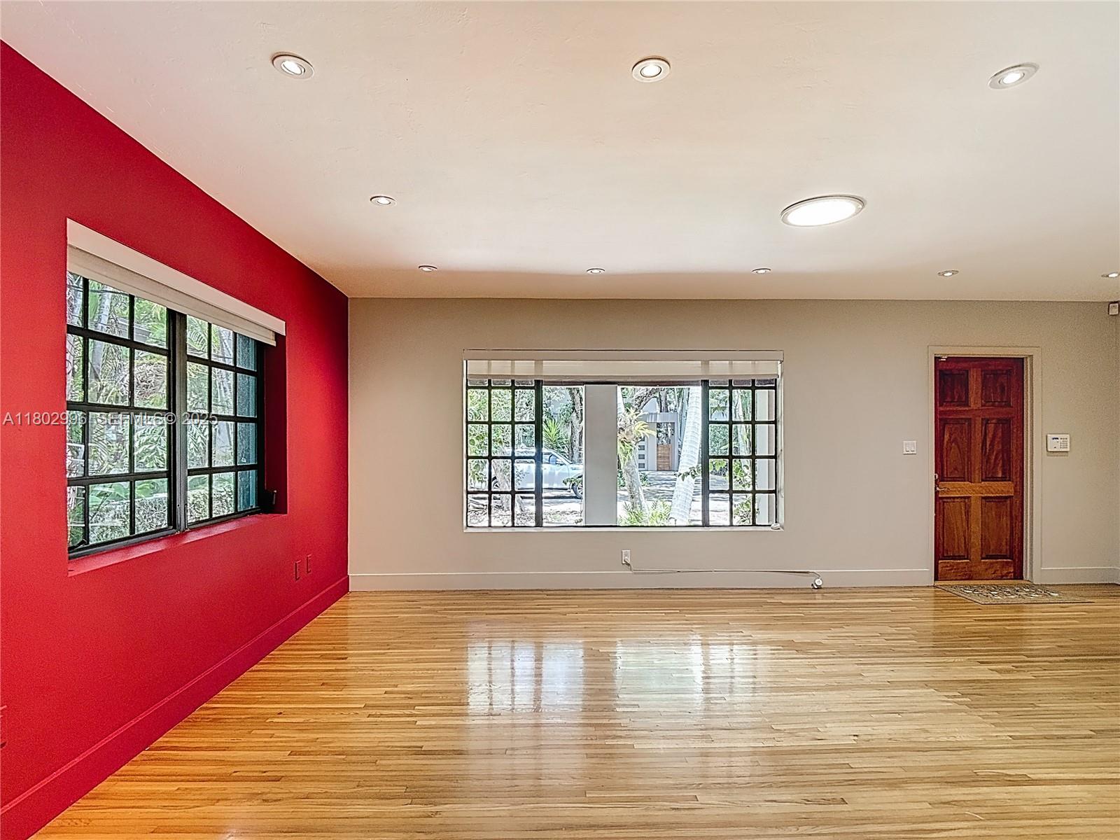A room with hardwood floors, a red accent wall, and two large grid-paneled windows — 2810 Crystal Ct, Miami FL 33133, MIAMI, FL