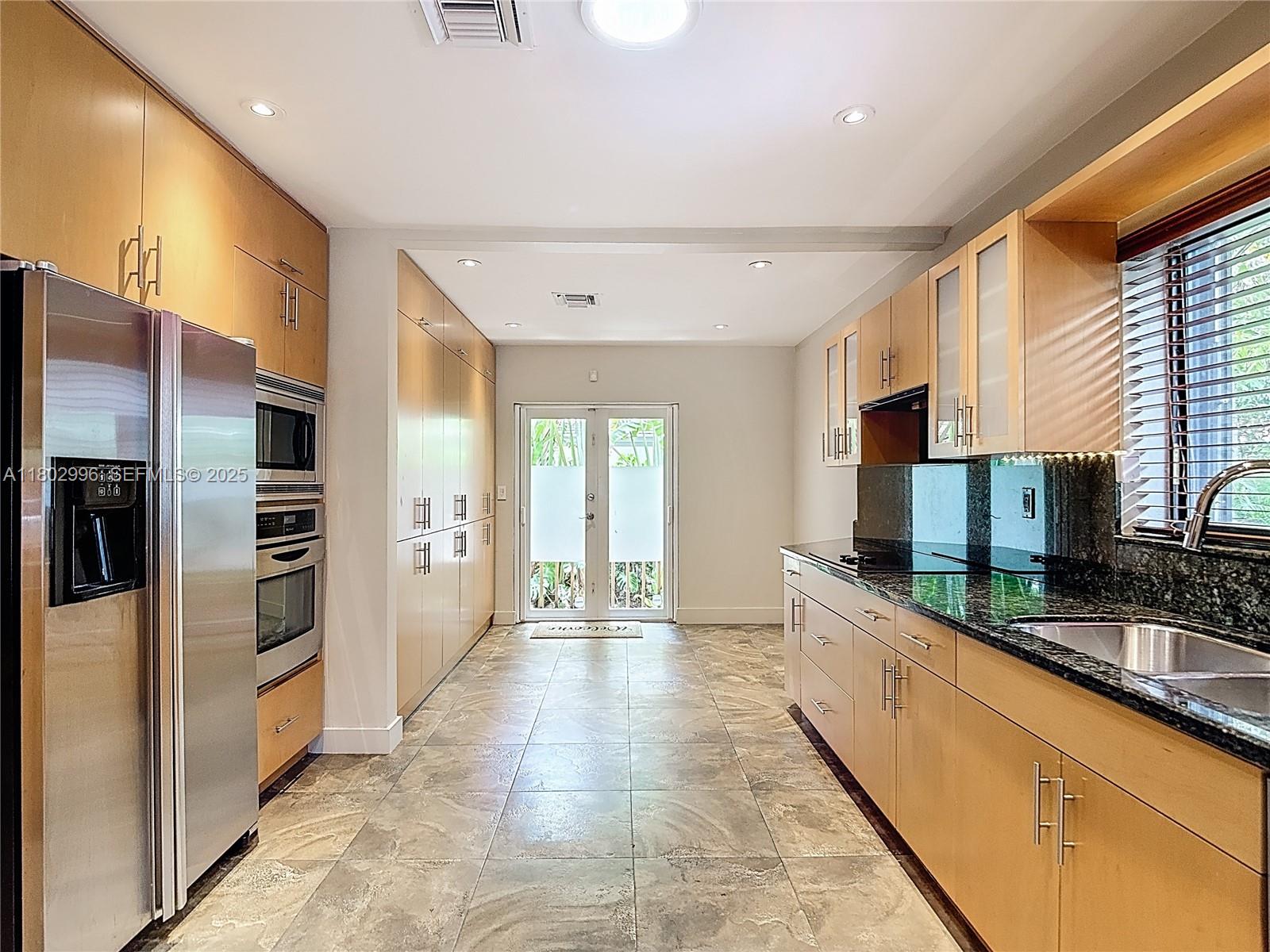 A galley kitchen features light wood cabinets, stainless steel appliances, granite countertops, and tile flooring — 2810 Crystal Ct, Miami FL 33133, MIAMI, FL