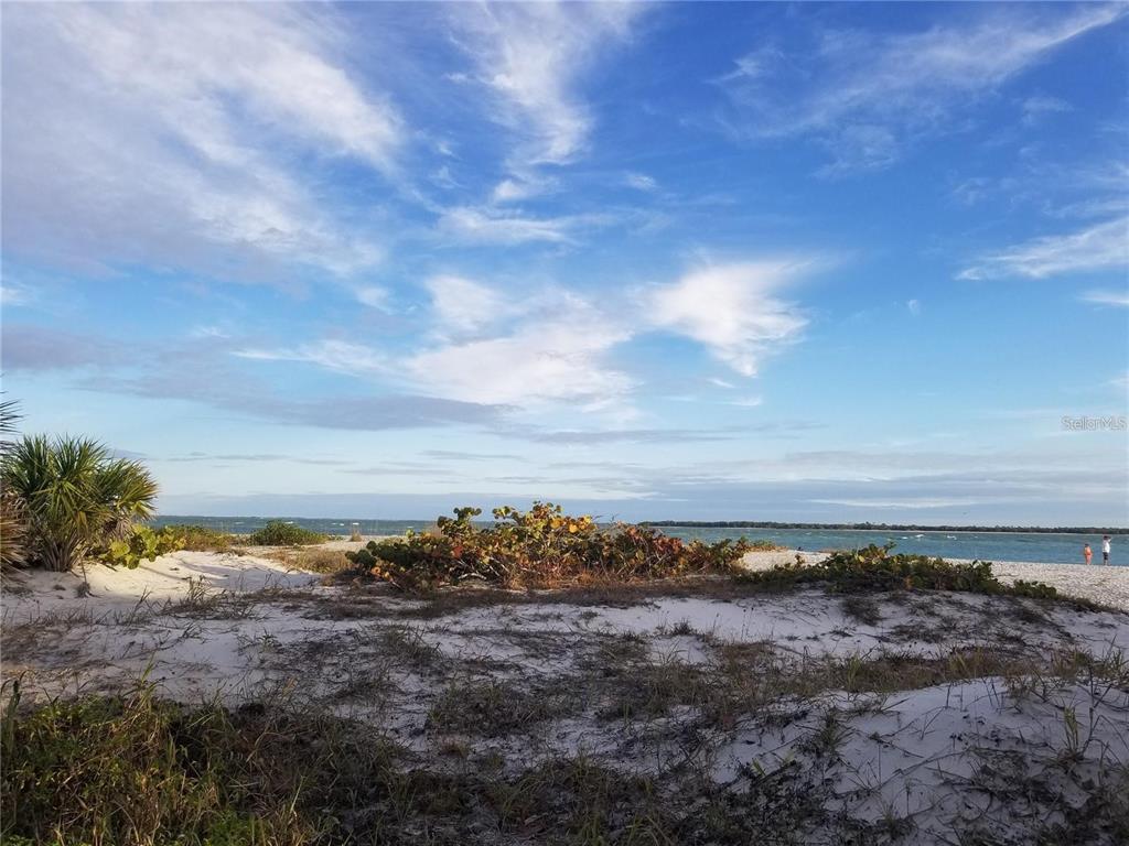 A sandy beach with dunes, coastal vegetation, and a view of the ocean under blue skies — 13362 CHAMBERLAIN BOULEVARD, PORT CHARLOTTE, FL