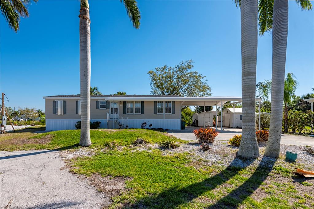 A single-story manufactured home with a carport, light siding, and palm trees in the yard — 3004 BAMBOO COURT, PUNTA GORDA, FL