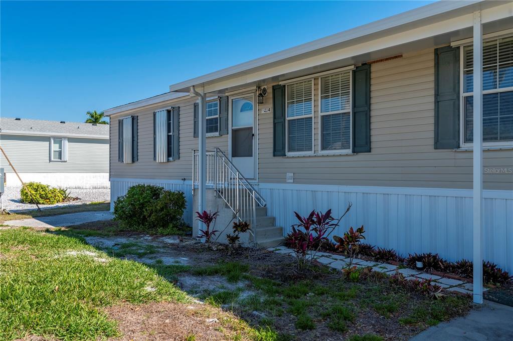 A tan manufactured home features a front entrance with stairs, a metal railing, and landscaping — 3004 BAMBOO COURT, PUNTA GORDA, FL
