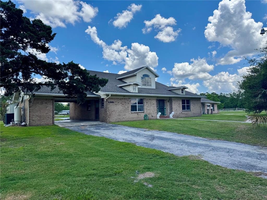 A brick house with a carport, a dormer window, and a paved driveway under a blue sky — 14371 US HIGHWAY 301 S, STARKE, FL
