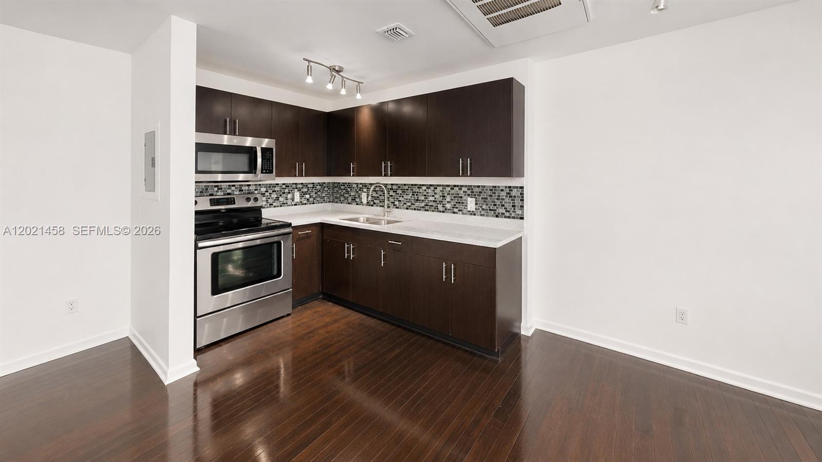 A kitchen features dark wood cabinets, stainless steel appliances, and a mosaic tile backsplash — 1542 Drexel Ave # 105, Miami Beach FL 33139, MIAMI BEACH, FL