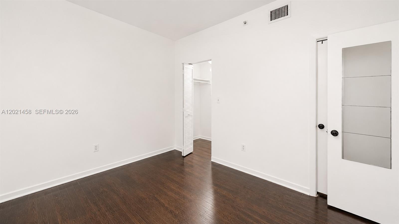 A room with dark wood flooring, white walls, a closet, and a door with glass panels — 1542 Drexel Ave # 105, Miami Beach FL 33139, MIAMI BEACH, FL