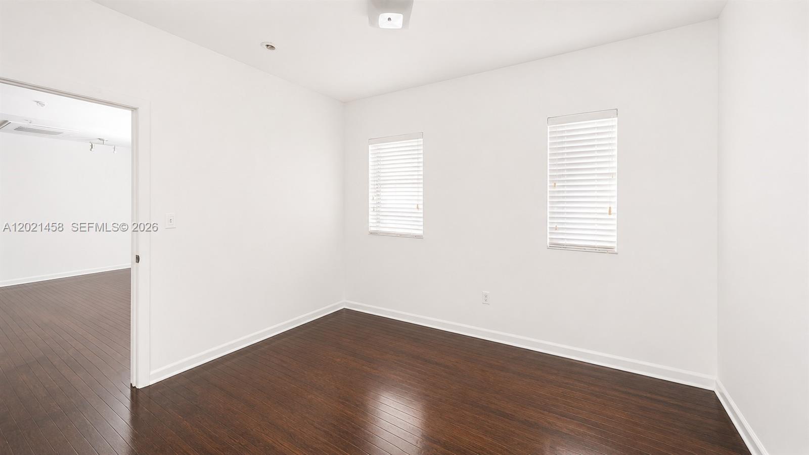 An empty room features white walls, dark wood flooring, and two windows with blinds — 1542 Drexel Ave # 105, Miami Beach FL 33139, MIAMI BEACH, FL