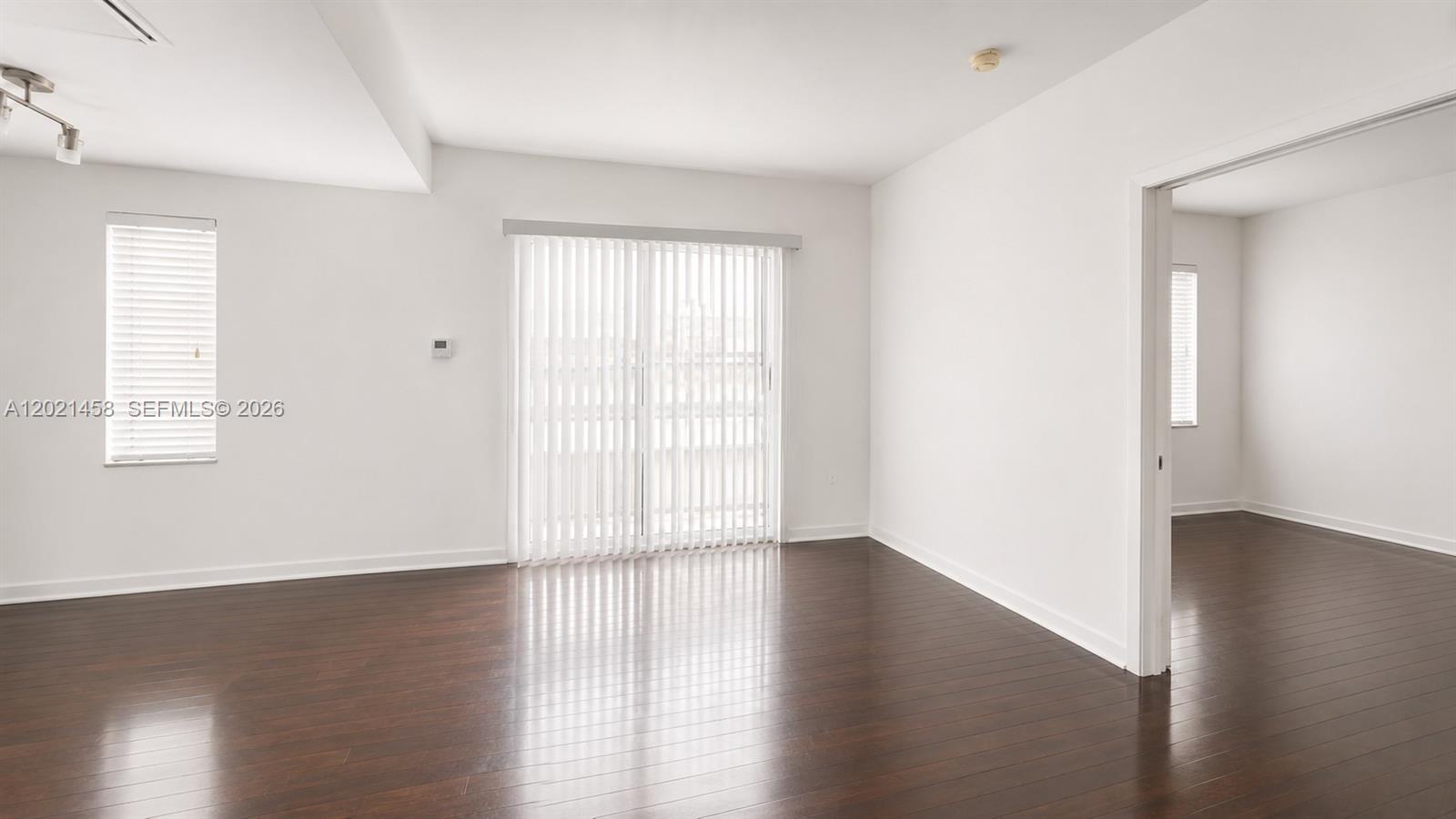 An empty room with dark wood flooring, white walls, and a sliding glass door — 1542 Drexel Ave # 105, Miami Beach FL 33139, MIAMI BEACH, FL