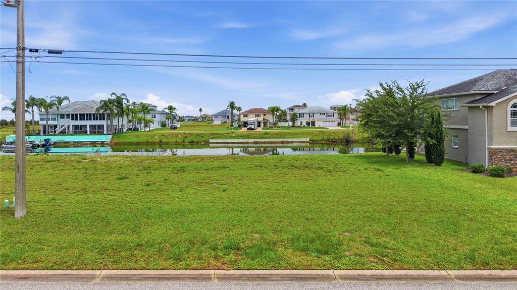 A vacant grassy lot sits in front of a canal with houses in the background — 3431 JEWFISH DRIVE, HERNANDO BEACH, FL