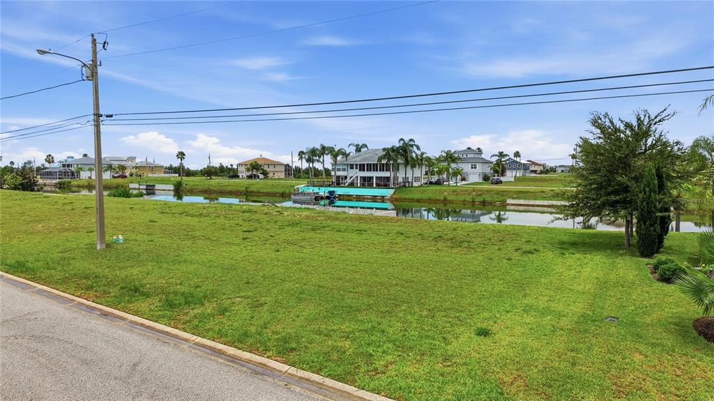 A grassy vacant lot overlooks a canal with several houses in the background — 3431 JEWFISH DRIVE, HERNANDO BEACH, FL