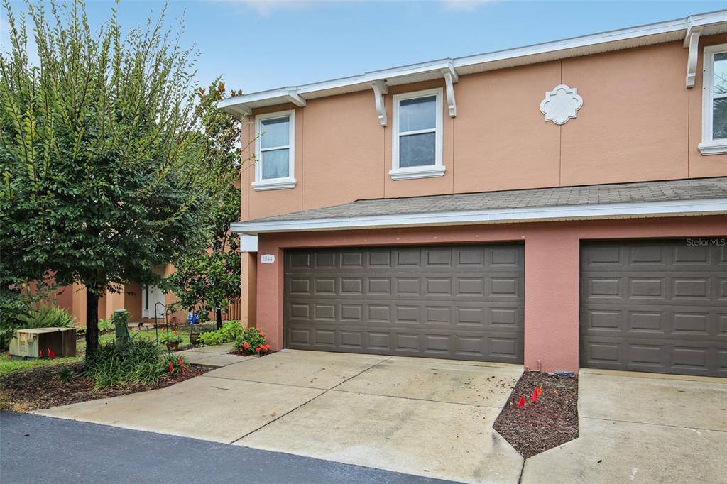 A two-story townhouse exterior with a two-car garage and tan stucco siding — 1844 SOMMARIE WAY, TARPON SPRINGS, FL