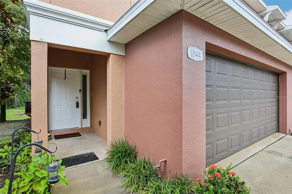 A view of a home exterior featuring a white front door and a garage door — 1844 SOMMARIE WAY, TARPON SPRINGS, FL