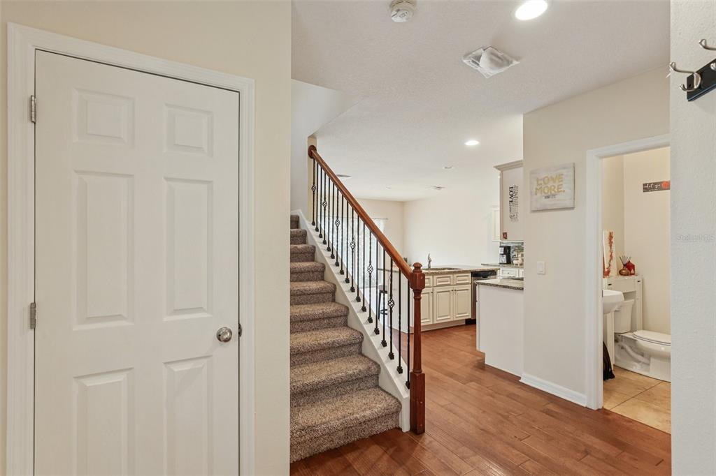 An interior view shows a carpeted staircase, wood flooring, a kitchen, and a half bathroom — 1844 SOMMARIE WAY, TARPON SPRINGS, FL