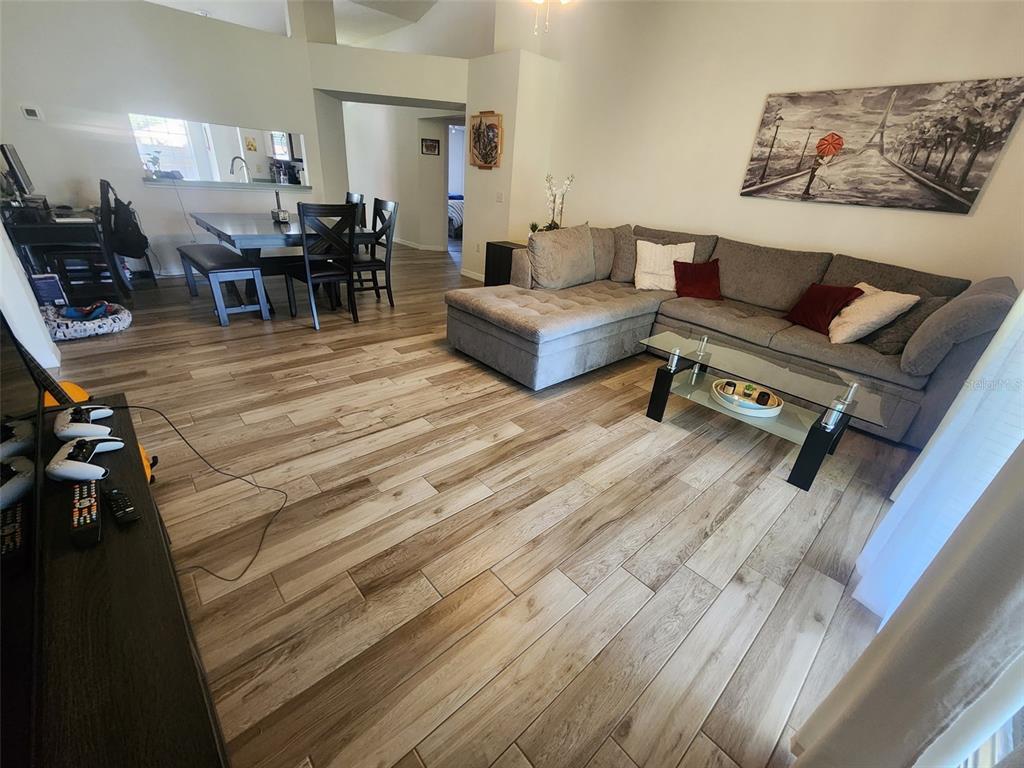 A living room with wood-look tile flooring, a sectional sofa, and an adjacent dining area — 2601 SUNDANCE CIRCLE, MULBERRY, FL