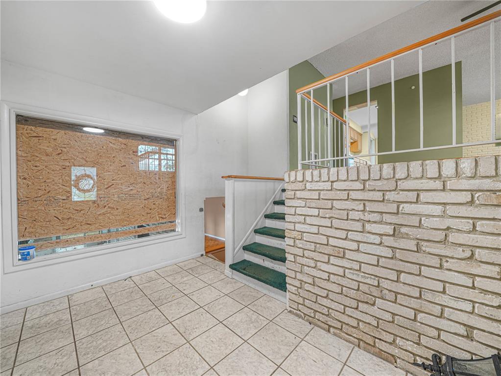 An entryway features tiled flooring, a brick wall, a staircase, and a boarded-up window — 129 LAKE OTIS ROAD SE, WINTER HAVEN, FL