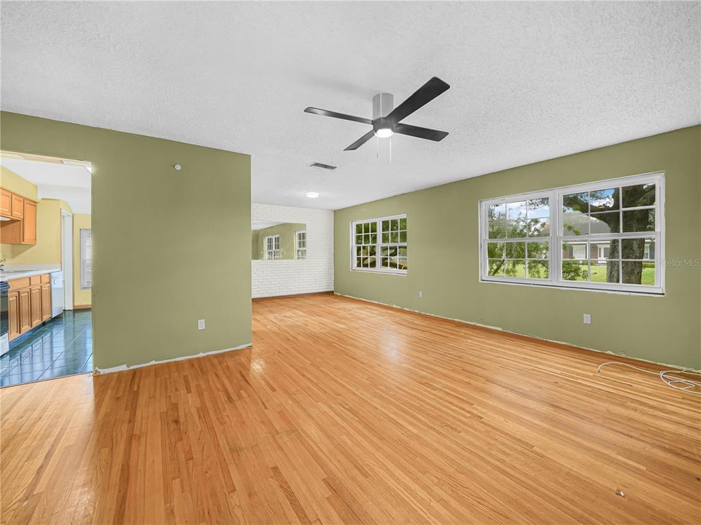 An empty living room features light green walls, hardwood floors, and a ceiling fan — 129 LAKE OTIS ROAD SE, WINTER HAVEN, FL