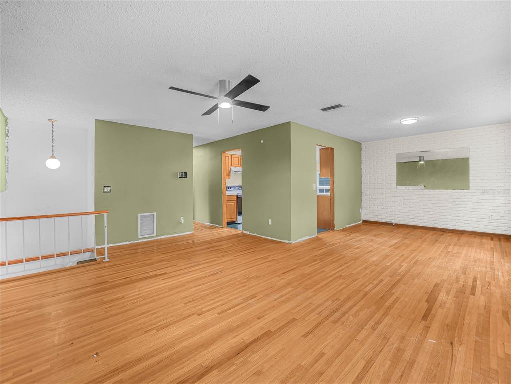 An open living area features hardwood floors, a green accent wall, and a white brick wall — 129 LAKE OTIS ROAD SE, WINTER HAVEN, FL