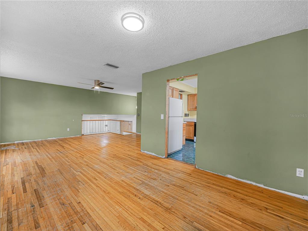 An interior view shows a living area with hardwood floors, olive walls, and a kitchen doorway — 129 LAKE OTIS ROAD SE, WINTER HAVEN, FL