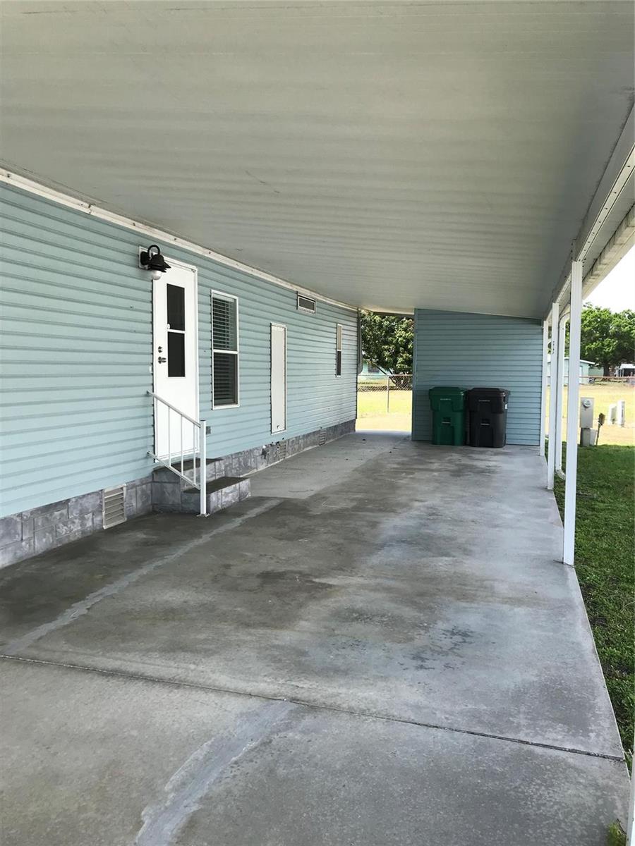 A light blue mobile home features a concrete carport and a white entry door — 1703 SW 35th Circle, Okeechobee FL 34974, OKEECHOBEE, FL