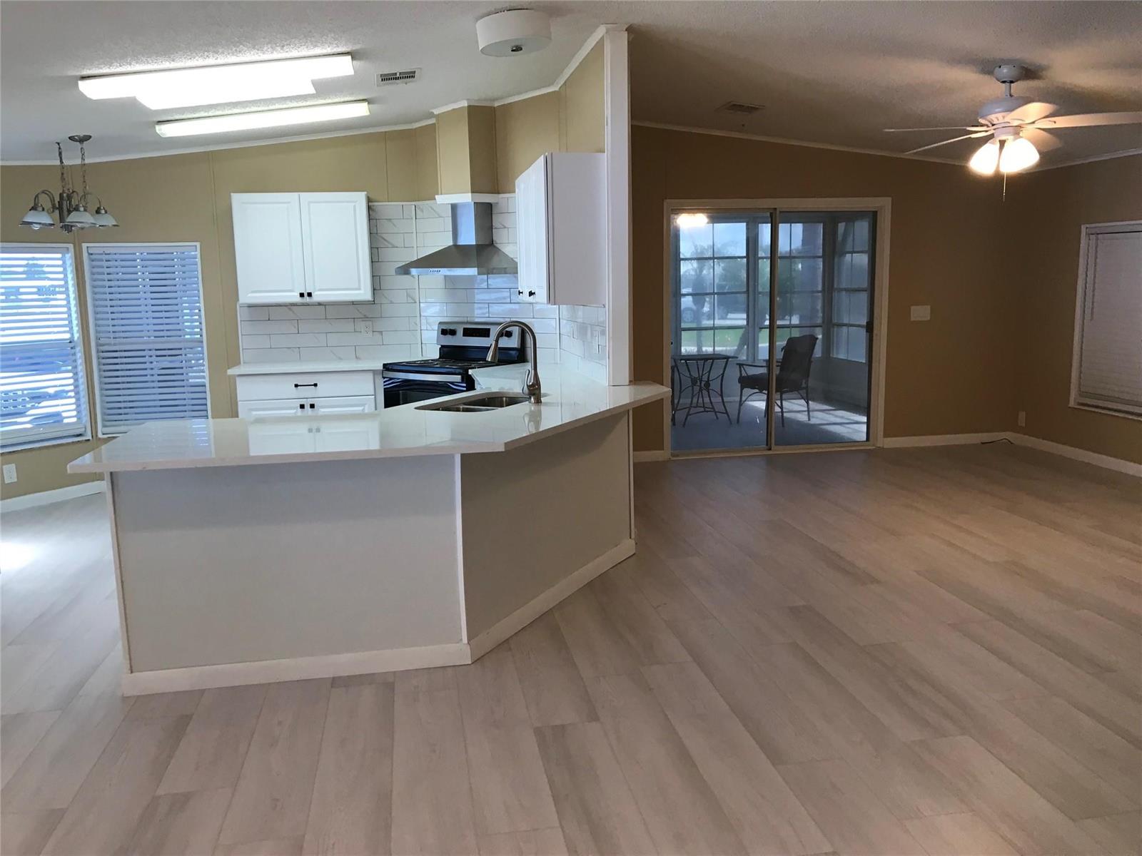A kitchen with white cabinets and countertops opens into a living area with wood flooring — 1703 SW 35th Circle, Okeechobee FL 34974, OKEECHOBEE, FL