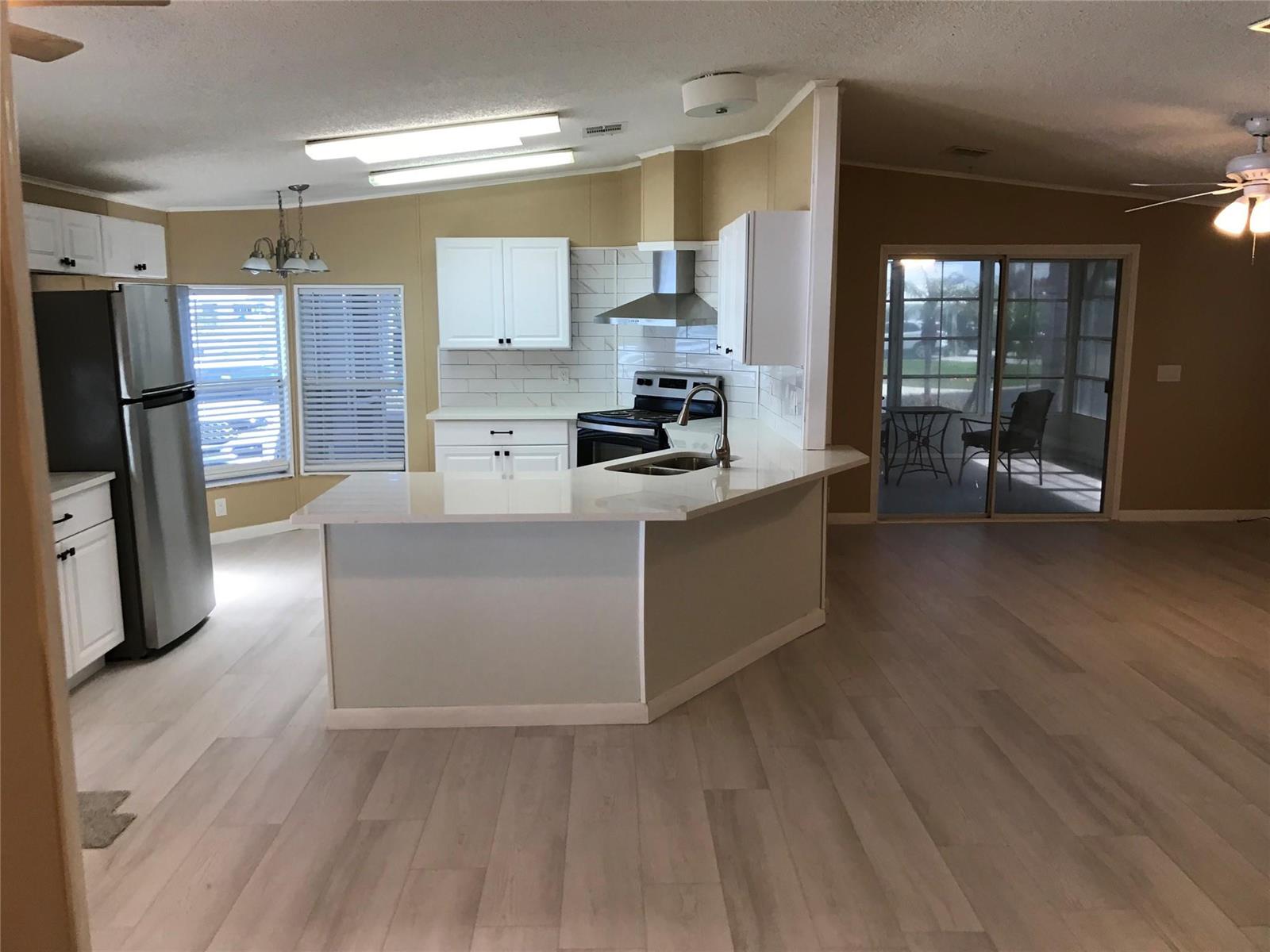 A kitchen with white cabinets, stainless steel appliances, and a peninsula counter overlooks a patio — 1703 SW 35th Circle, Okeechobee FL 34974, OKEECHOBEE, FL