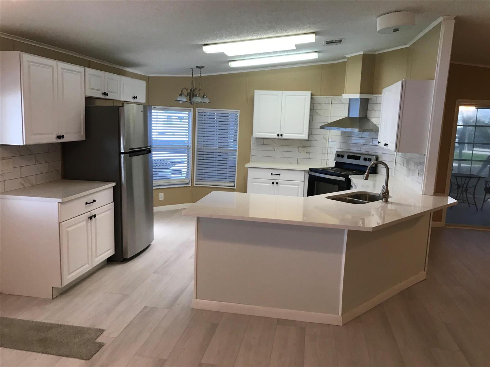 A kitchen features white cabinets, stainless steel appliances, a peninsula, and light-colored wood flooring — 1703 SW 35th Circle, Okeechobee FL 34974, OKEECHOBEE, FL