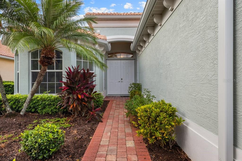 A brick walkway leads to the double front doors of a house with stucco walls — 3927 WHISPERING OAKS DRIVE, NORTH PORT, FL