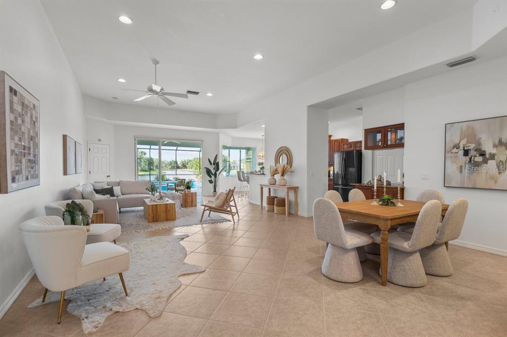 An open-concept living and dining area with tile floors, neutral furniture, and a pool view — 3927 WHISPERING OAKS DRIVE, NORTH PORT, FL