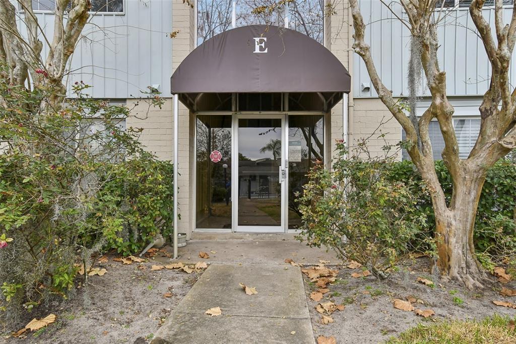 The exterior entrance to building E features a brown awning over a glass door — 1695 LEE ROAD UNIT E115, WINTER PARK, FL