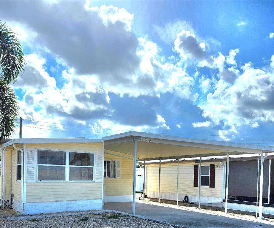 A yellow mobile home features a large attached carport and a gravel front yard — 6509 OREGON STREET, BRADENTON, FL