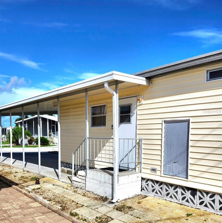 The exterior of a light yellow mobile home features a covered carport and metal skirting — 6509 OREGON STREET, BRADENTON, FL