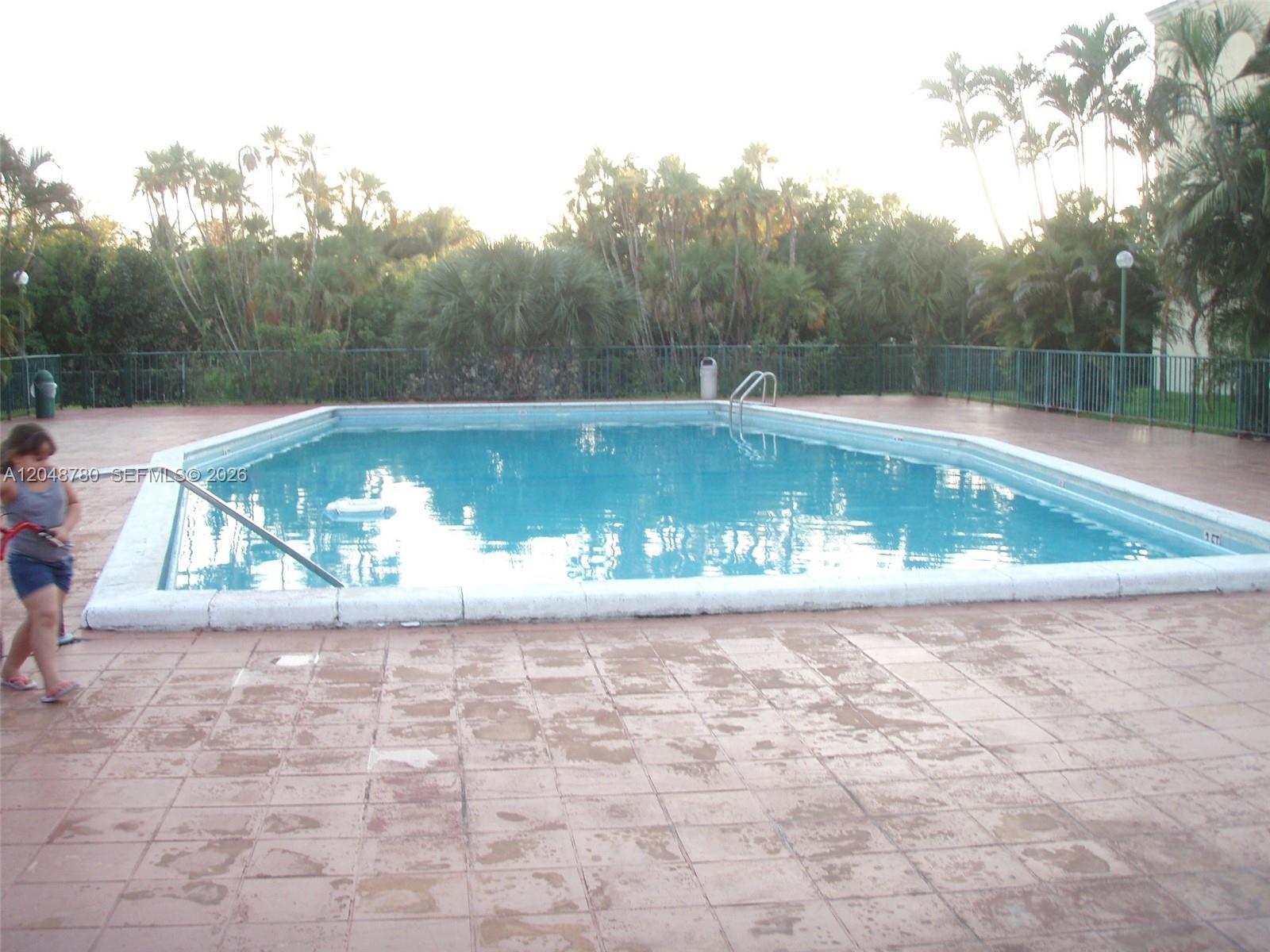 A rectangular swimming pool is surrounded by a tiled deck and a metal fence — 6980 NW 186th St # 522, Hialeah FL 33015, HIALEAH, FL