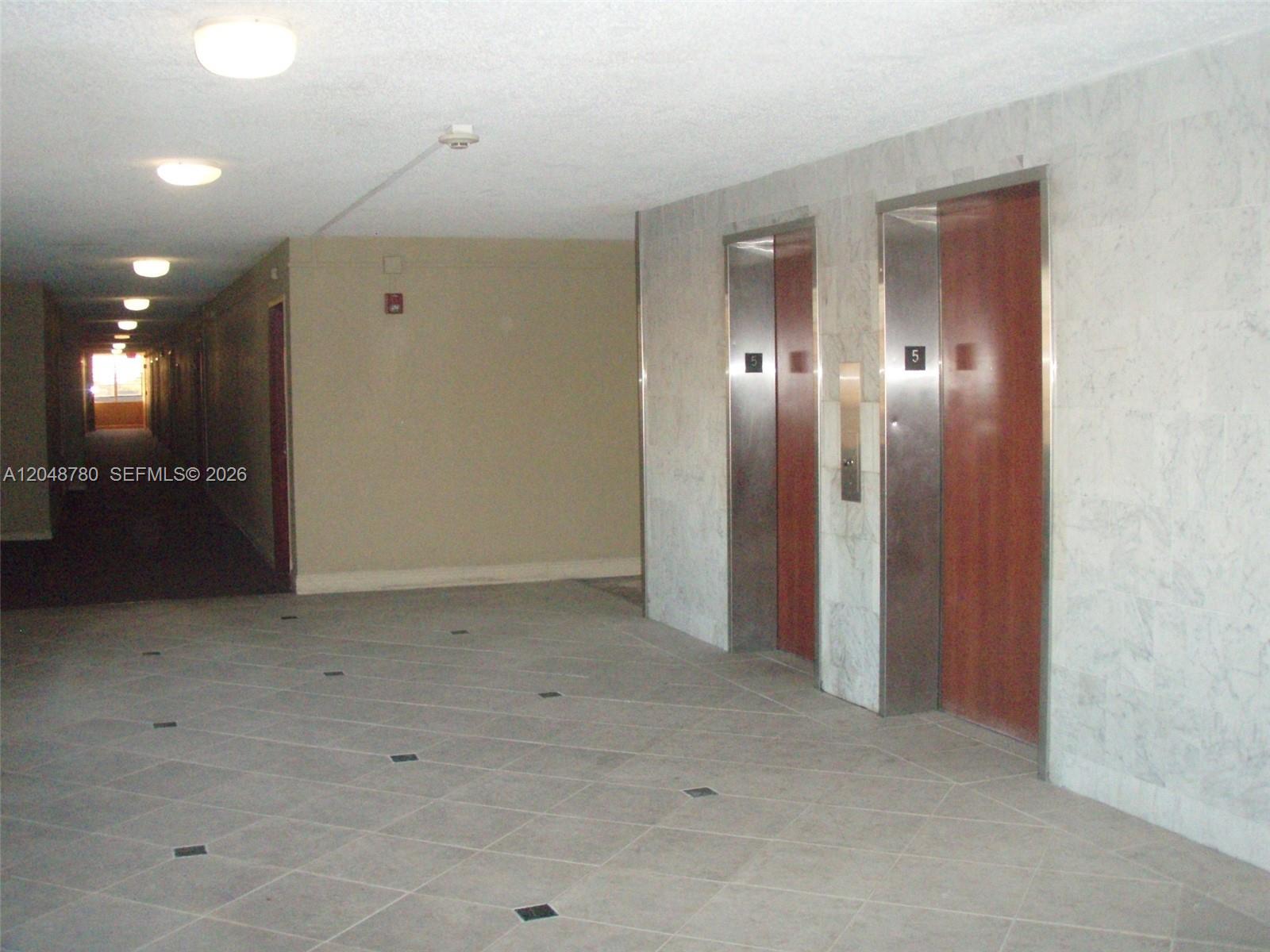 A hallway features two elevators with wood-paneled doors and marble-tiled walls — 6980 NW 186th St # 522, Hialeah FL 33015, HIALEAH, FL
