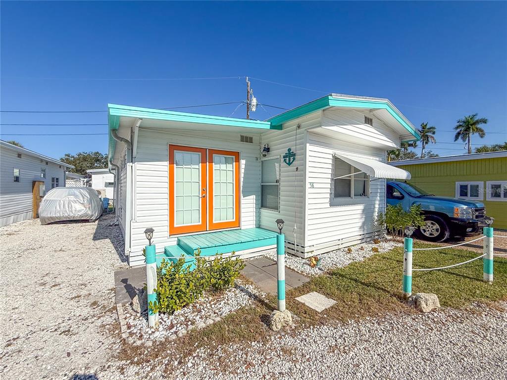 A white mobile home with turquoise trim and orange double doors sits on a gravel lot — 12507 CORTEZ ROAD W UNIT 58, CORTEZ, FL