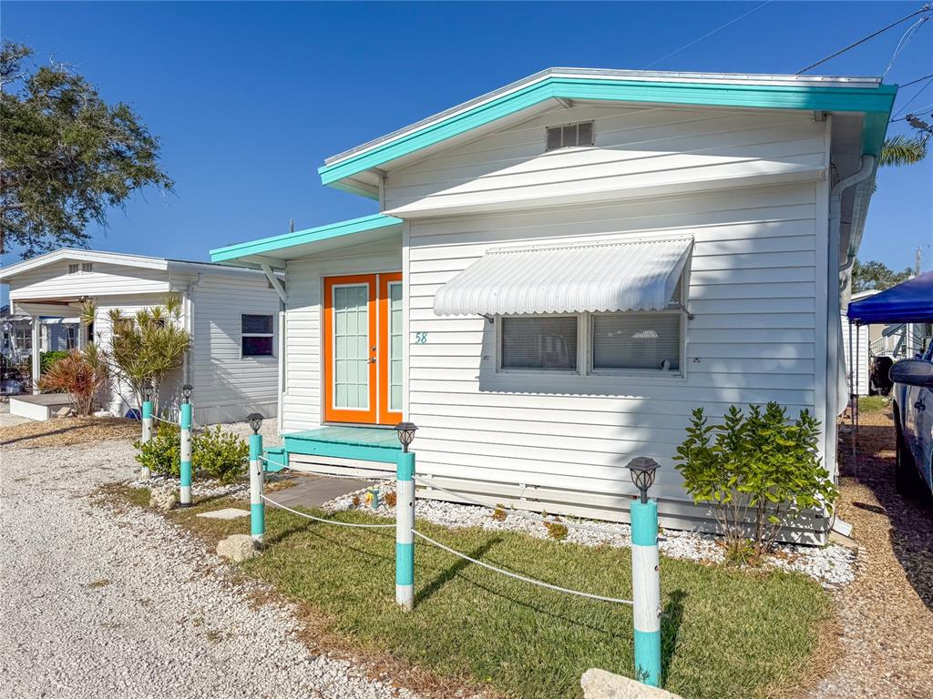 A white mobile home with turquoise trim and bright orange double doors sits on gravel — 12507 CORTEZ ROAD W UNIT 58, CORTEZ, FL