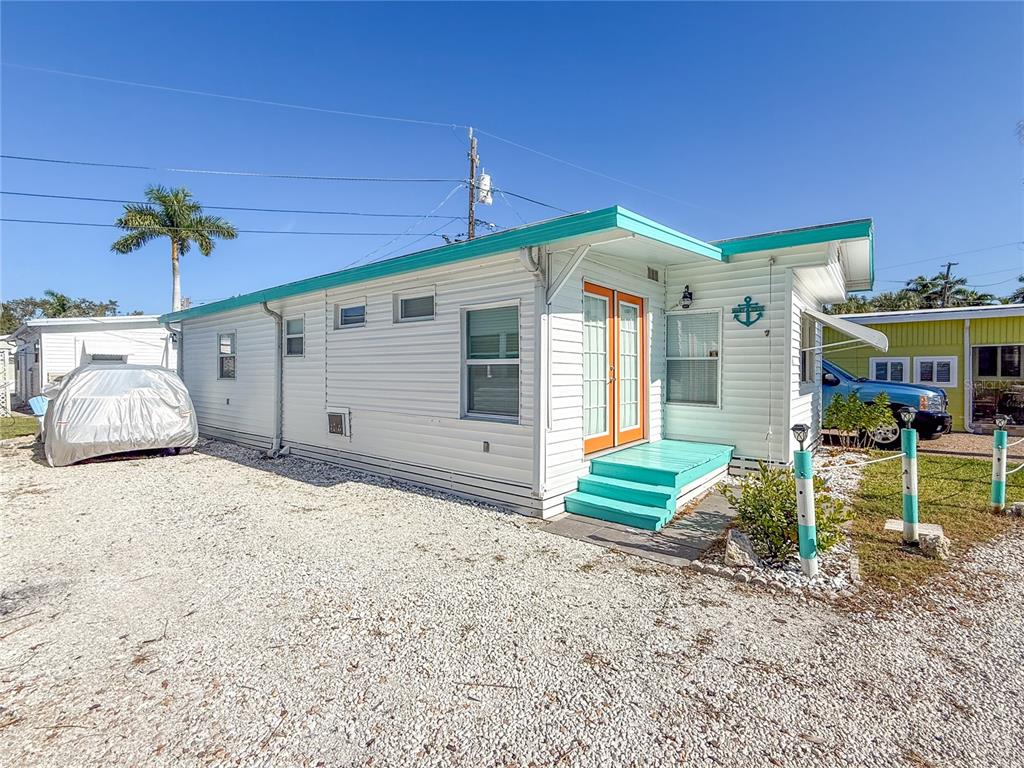 A white mobile home with teal trim and orange doors sits on a gravel lot — 12507 CORTEZ ROAD W UNIT 58, CORTEZ, FL