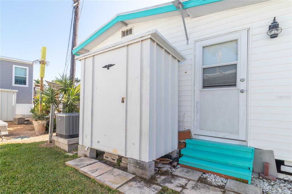 A white exterior storage shed sits next to a house with a turquoise-painted door and steps — 12507 CORTEZ ROAD W UNIT 58, CORTEZ, FL