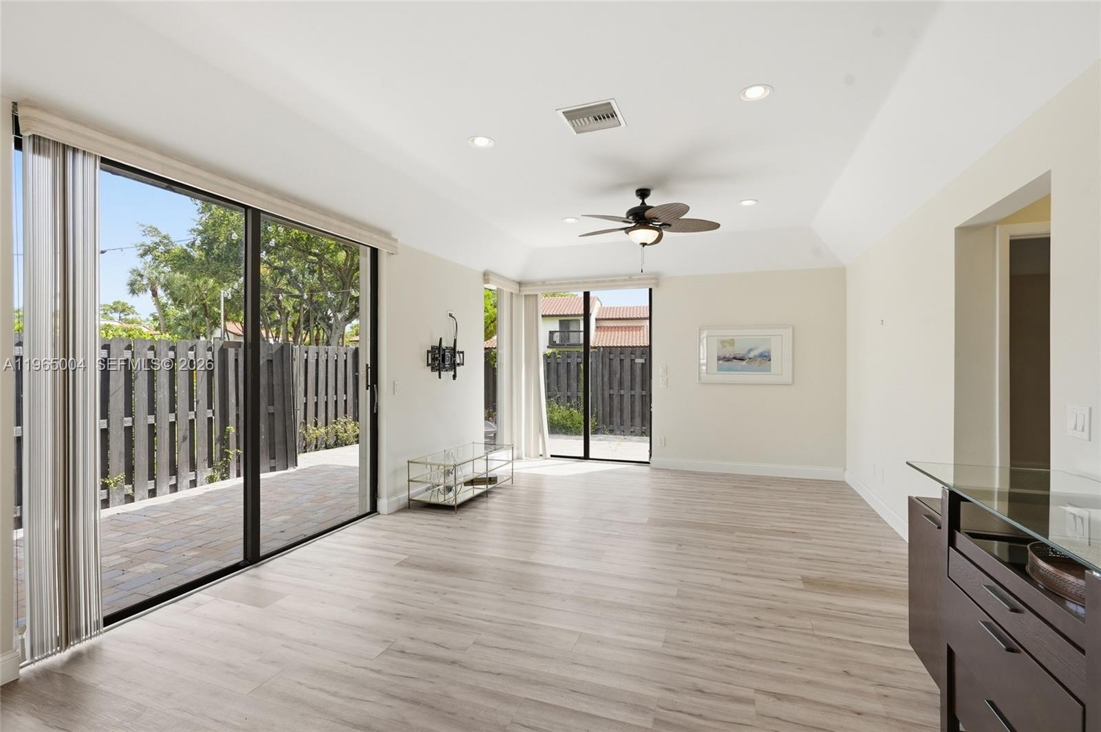 A bright living room features light wood-look flooring, a ceiling fan, and sliding glass doors — 5726 Fox Hollow Dr # A, Boca Raton FL 33486, BOCA RATON, FL