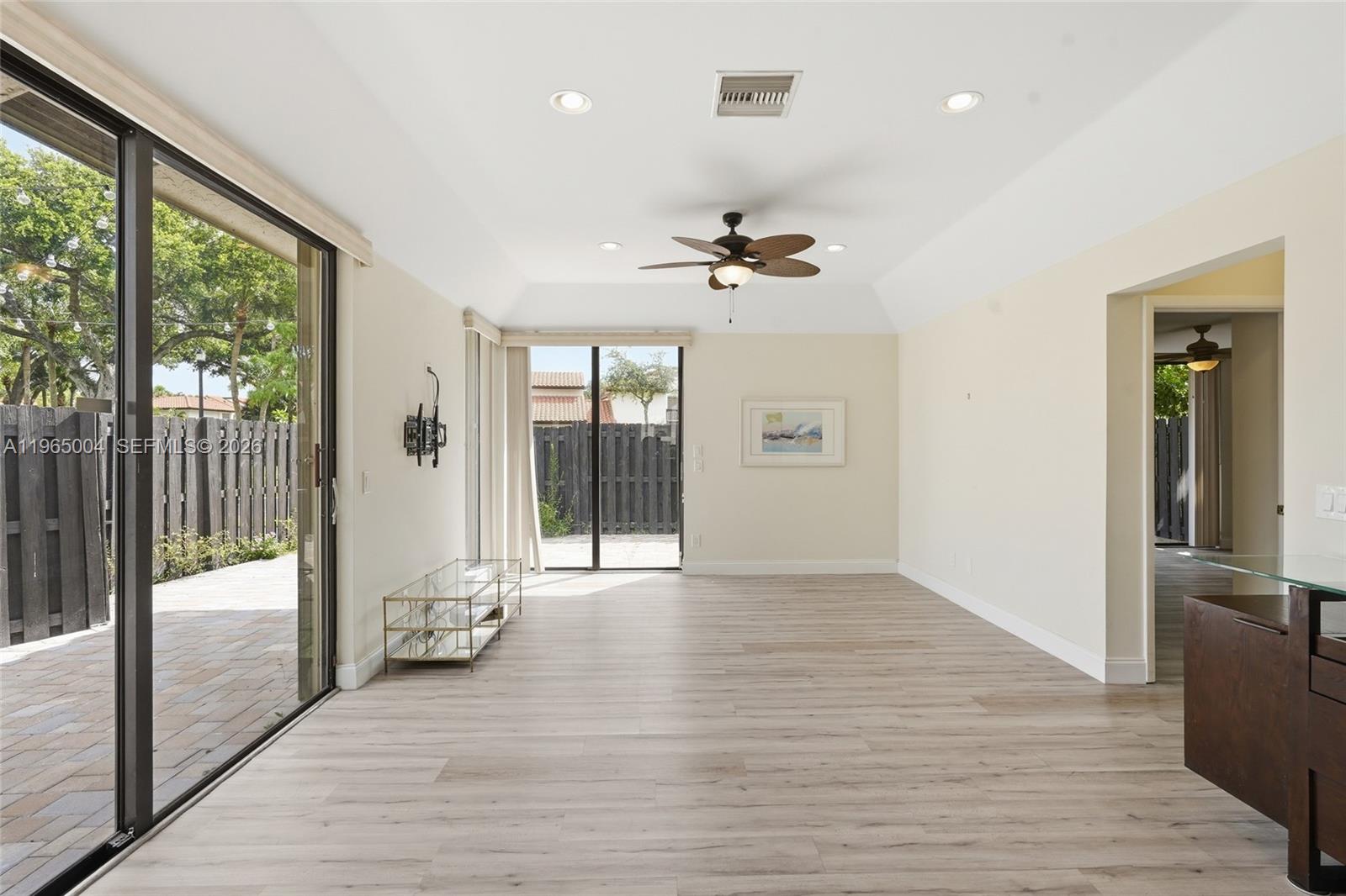 A bright living room features light wood flooring, a tray ceiling, and sliding glass doors — 5726 Fox Hollow Dr # A, Boca Raton FL 33486, BOCA RATON, FL