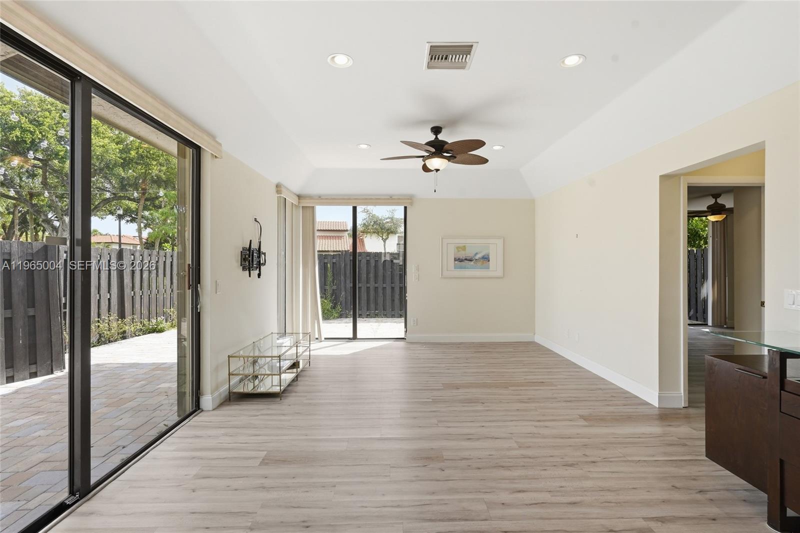A bright living room features light wood-look flooring, a tray ceiling, and sliding glass doors — 5726 Fox Hollow Dr # A, Boca Raton FL 33486, BOCA RATON, FL