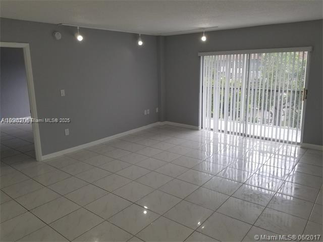 An empty room with gray walls, white tiled floors, and a sliding glass balcony door — 4160 Inverrary Dr # 505, Lauderhill FL 33319, LAUDERHILL, FL