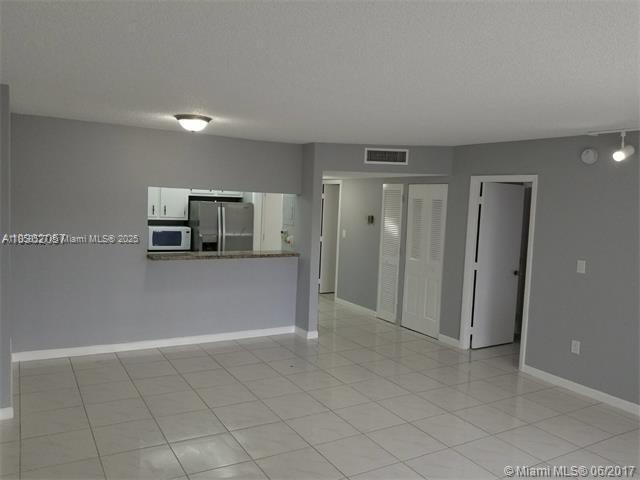 A living area with light-colored tile flooring, gray walls, and a kitchen pass-through window — 4160 Inverrary Dr # 505, Lauderhill FL 33319, LAUDERHILL, FL